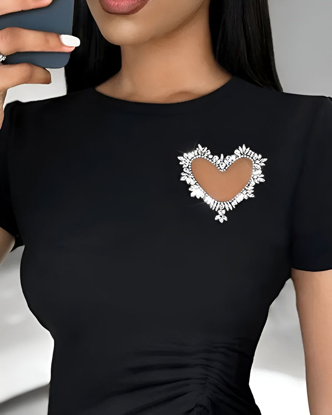 Une femme porte un t-shirt noir avec un cœur en strass découpé au niveau de la poitrine.