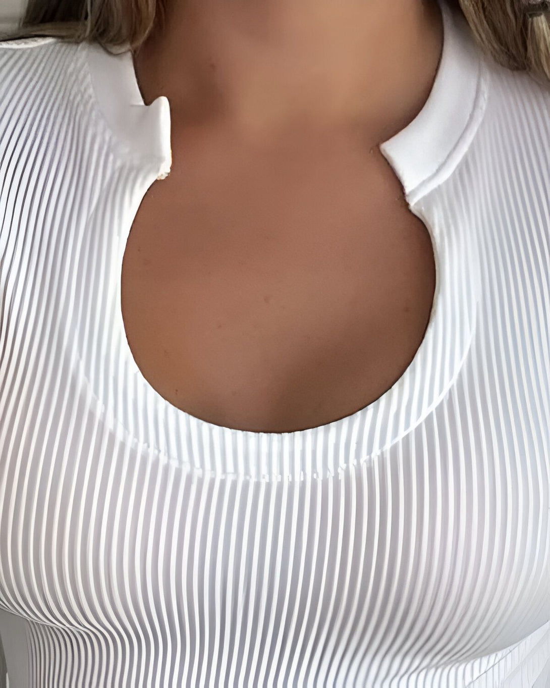 Une femme porte un haut blanc moulant avec un col rond. Le haut est côtelé et a des manches courtes.
