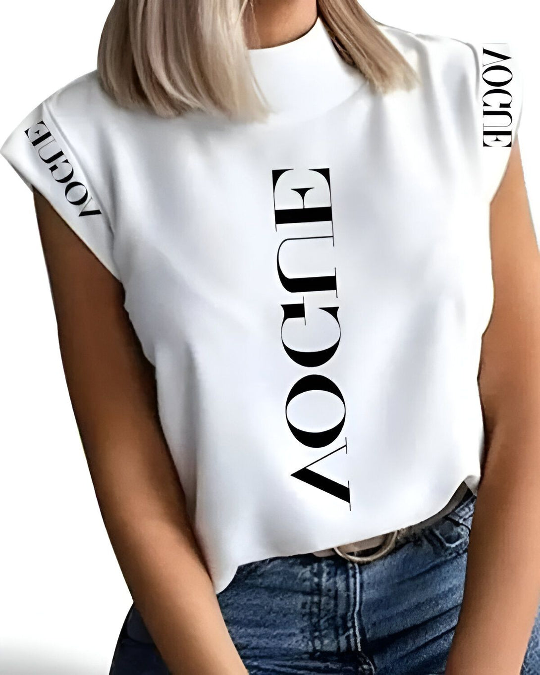 Une femme porte un t-shirt blanc avec le mot "Vogue" écrit en noir sur le devant. Le t-shirt est rentré dans un jean bleu. La femme a les cheveux blonds et les yeux bleus. Elle est souriante.