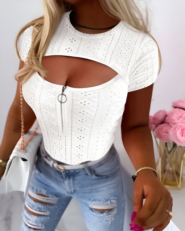 Une femme porte un haut blanc moulant avec un décolleté plongeant et des manches courtes. Elle porte également un jean bleu déchiré et des talons hauts.