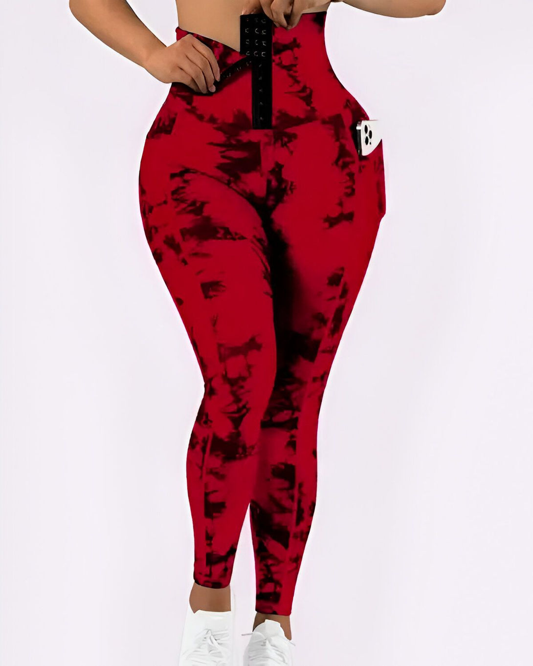 Une femme porte un legging rouge et noir tie-dye avec une ceinture corset. Elle a un téléphone dans la poche de son legging.