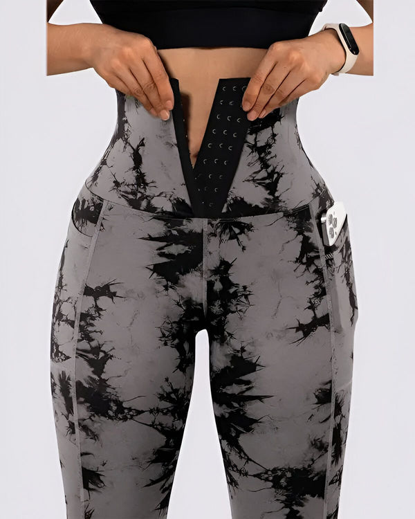 Une femme porte un legging taille haute gris et noir. Le legging est en matière stretch et possède une ceinture intégrée. La femme ajuste la ceinture pour qu'elle soit bien ajustée.