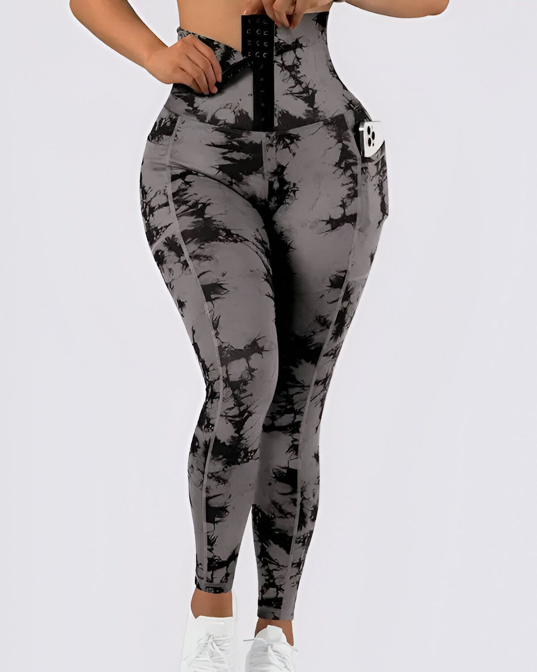 Une femme porte un legging taille haute gris et noir avec une ceinture intégrée. Elle ajuste la ceinture pour la serrer. Le legging est fabriqué dans un tissu extensible et confortable. Il est parfait pour le sport ou pour le quotidien.