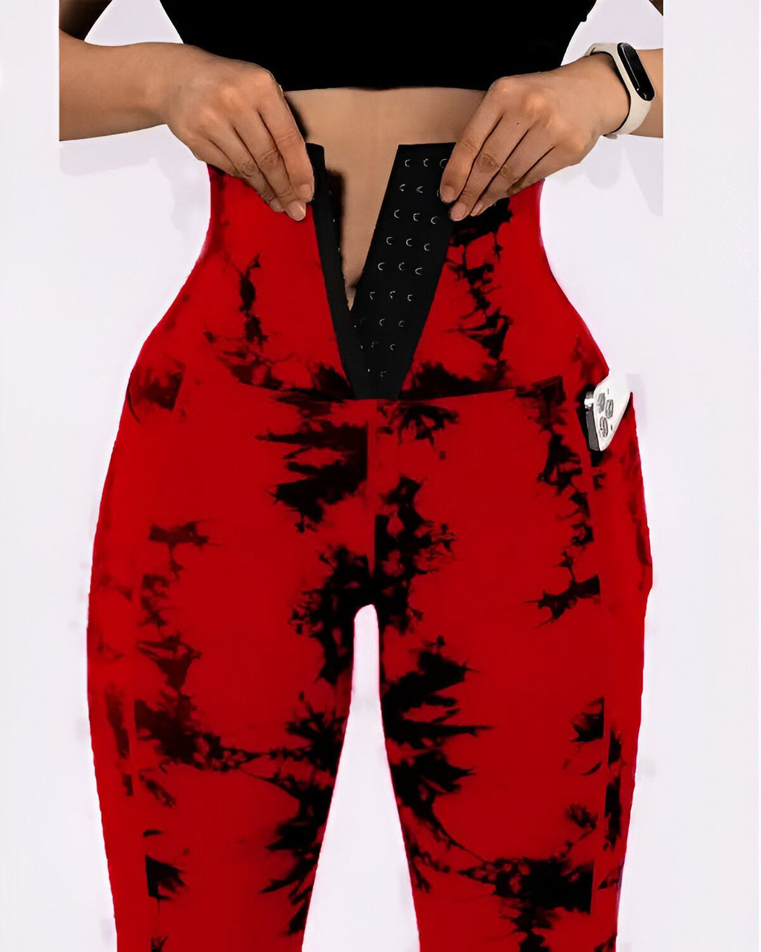 Une femme porte un legging rouge et noir tie-dye avec une taille haute et une fermeture à crochets. Elle porte également une montre connectée blanche à son poignet gauche.