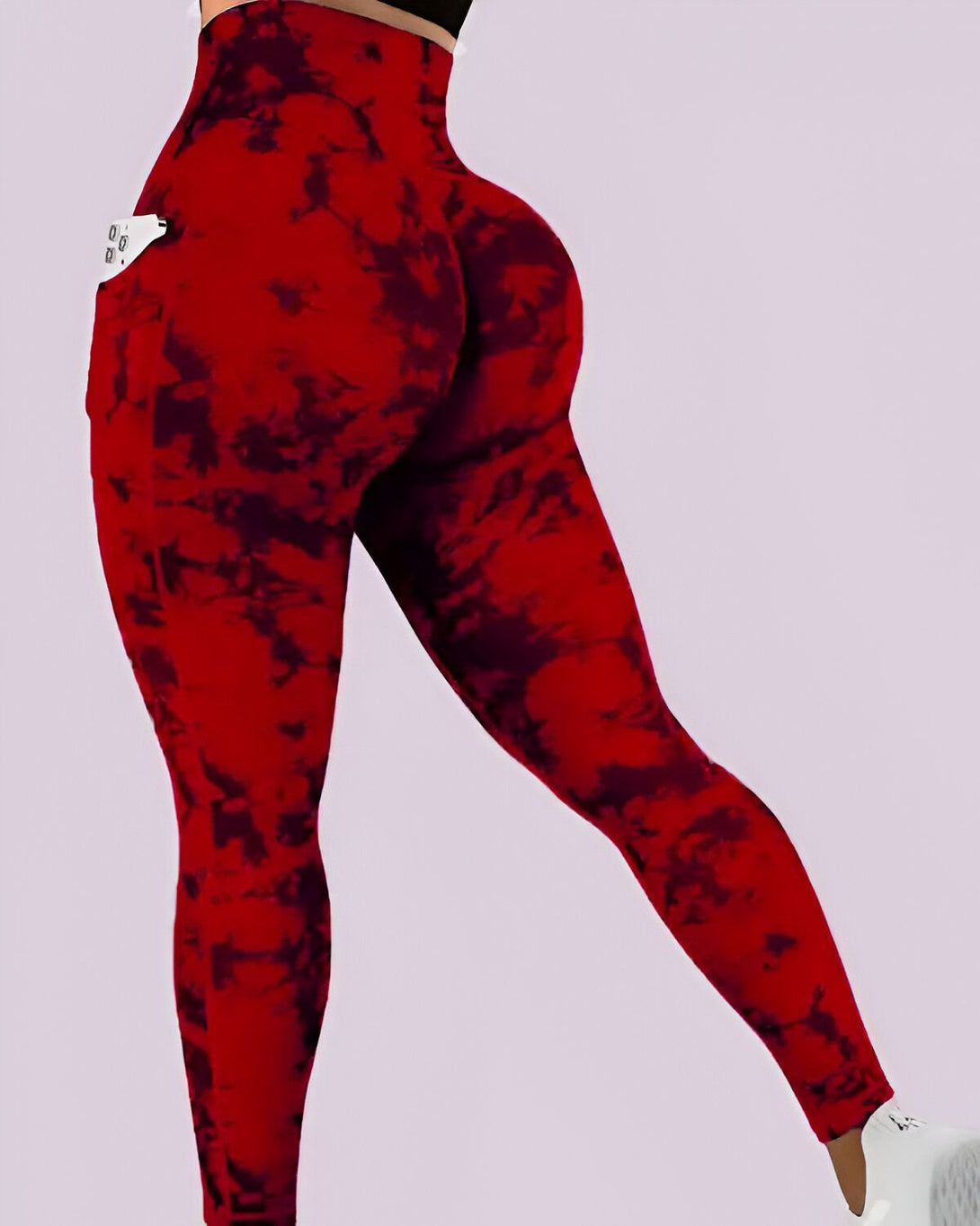Une femme porte un legging rouge et noir tie-dye avec une poche sur le côté. Le legging est taille haute et épouse les courbes du corps. La femme est vue de dos et porte des baskets blanches.