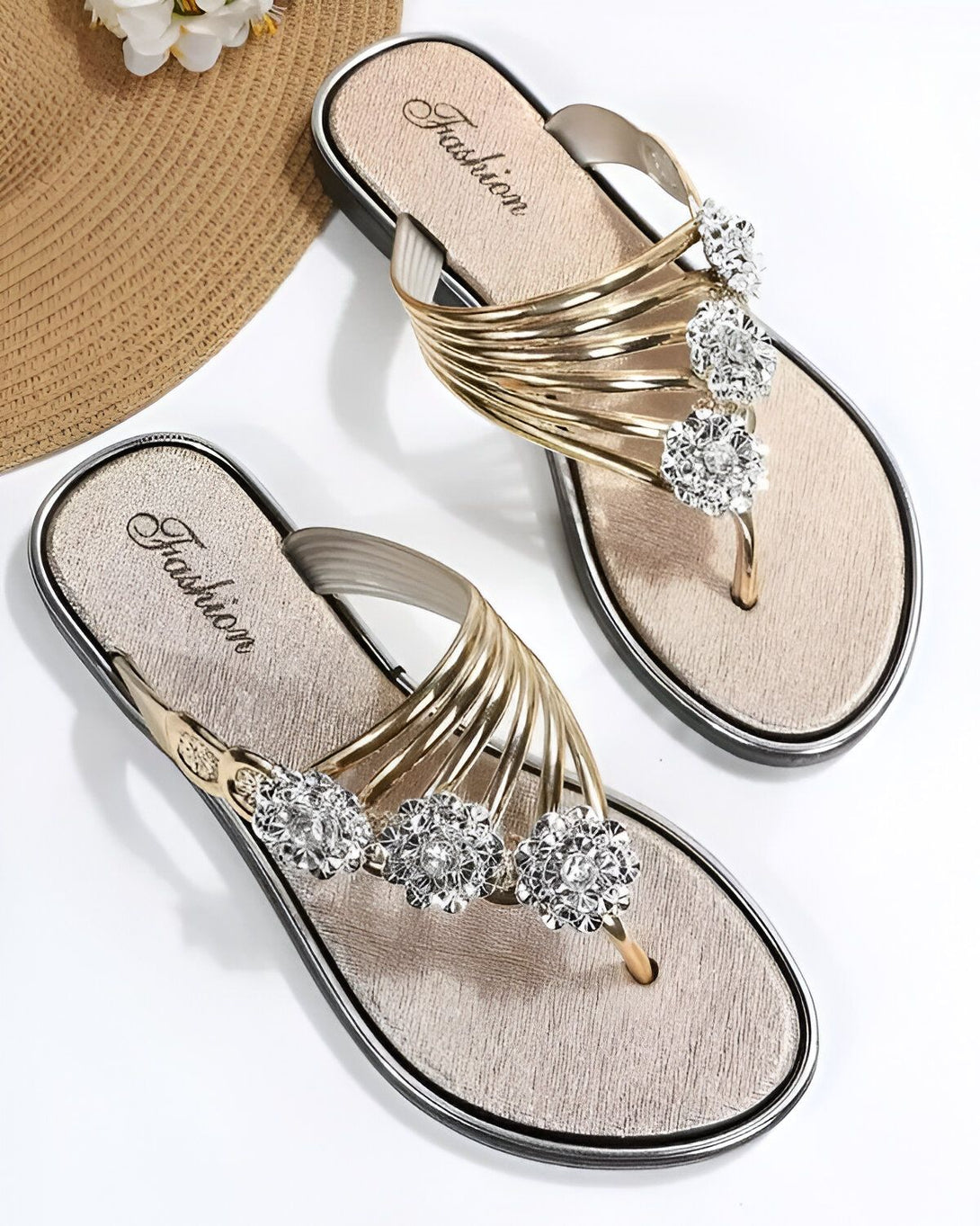 Une paire de tongs dorées pour femmes avec des fleurs en strass. Les tongs sont de la marque Fashion.