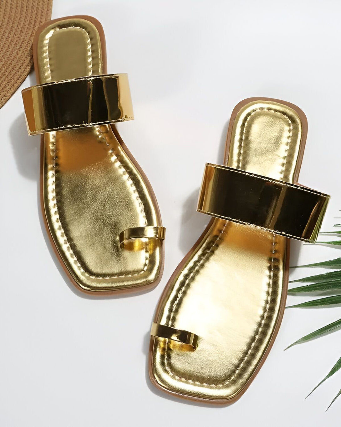 Une paire de sandales dorées métallisées. Les sandales sont plates et ont une bride qui passe entre le gros orteil et le deuxième orteil.