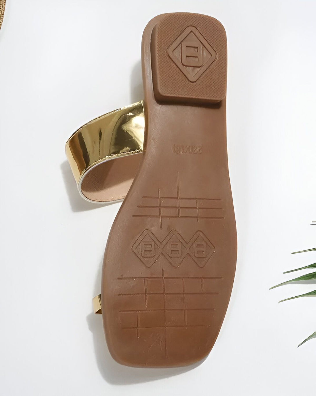 Une paire de sandales dorées pour femmes. Les sandales ont une semelle plate et une bride qui passe entre les orteils. La bride est ornée d'un logo doré.