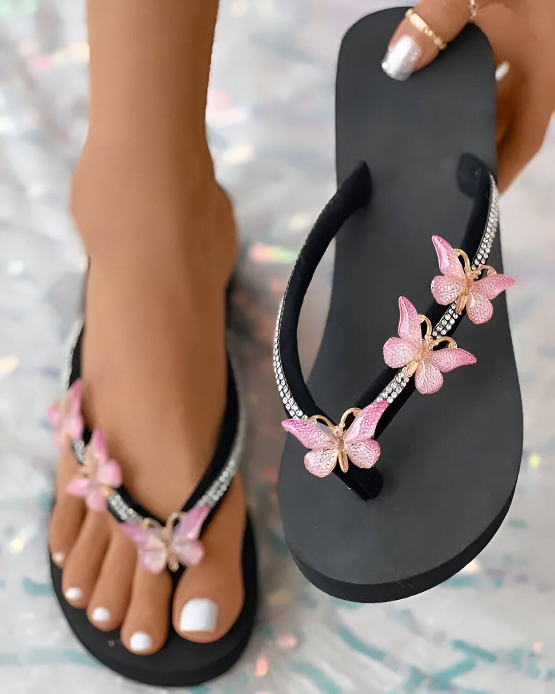 Une femme porte des tongs noires avec des papillons roses décorés de strass.