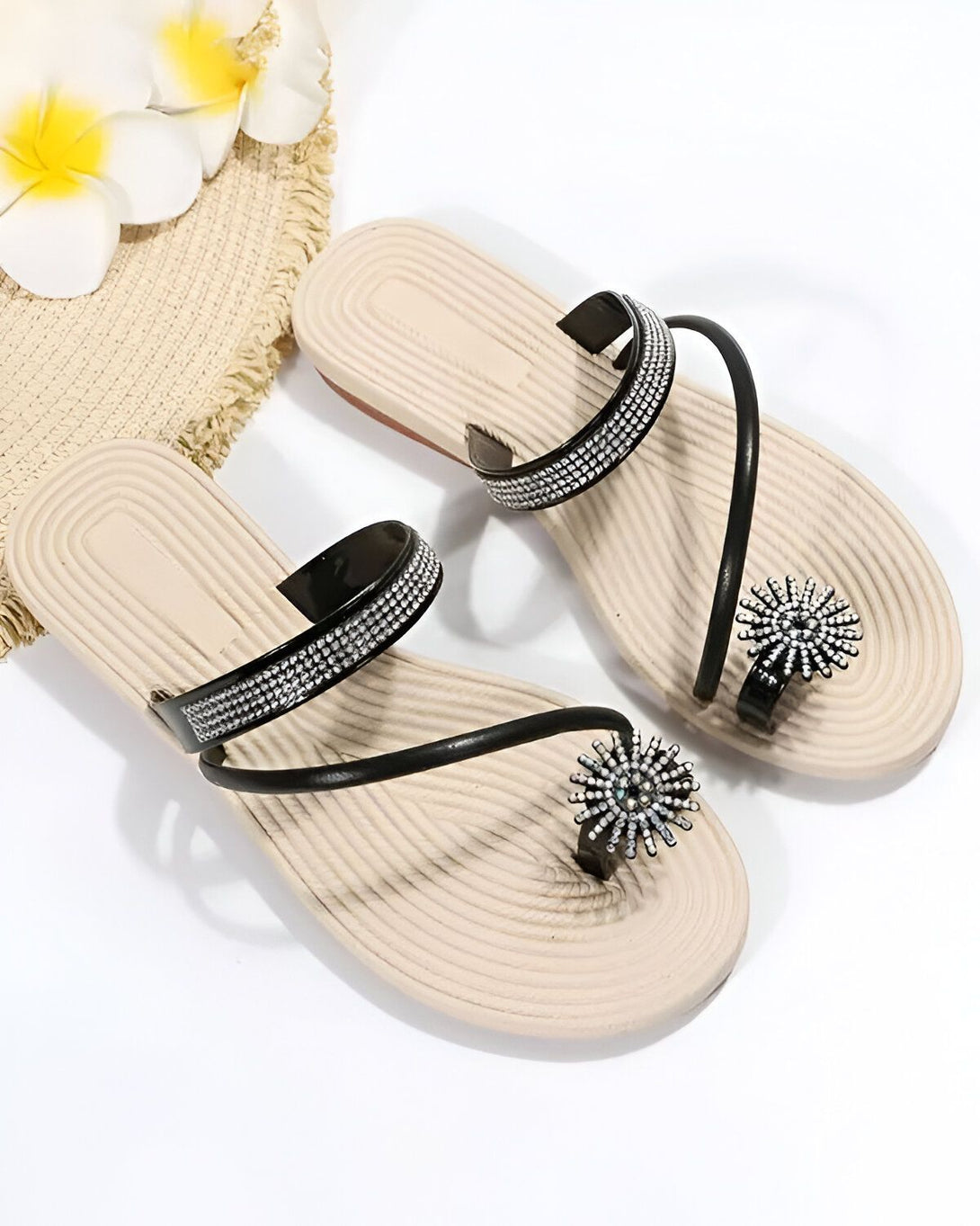 Une paire de tongs noires et blanches avec des strass. Les tongs sont ornées de fleurs en strass sur le dessus et ont une semelle beige.