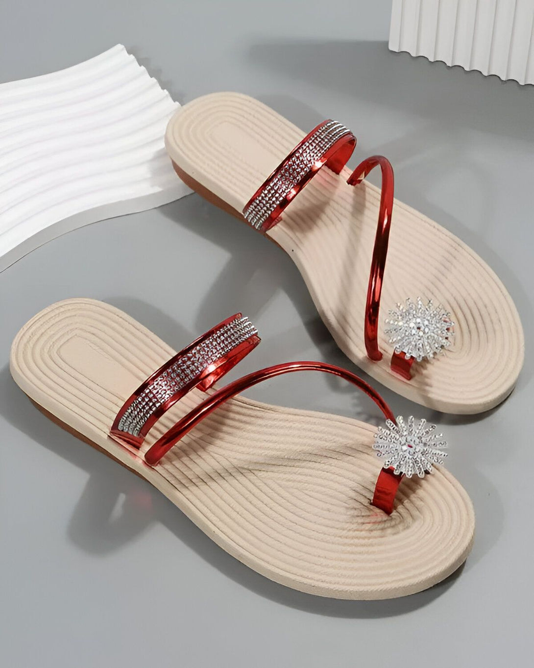 Une paire de tongs rouges avec des strass argentés sur le dessus et une fleur argentée sur le bout.
