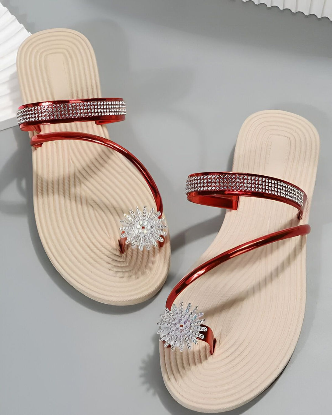 Une paire de tongs rouges et beiges pour femmes avec des strass en forme de fleur sur le dessus.