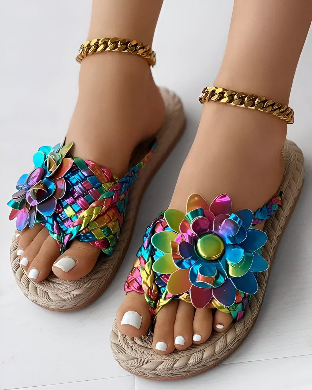 Une paire de sandales plates pour femmes avec des fleurs colorées. Les fleurs sont faites de plusieurs pétales de différentes couleurs, ce qui donne un effet arc-en-ciel. Les sandales sont faites de paille tressée, ce qui les rend légères et confortables à porter. La semelle intérieure est rembourrée, ce qui offre un confort supplémentaire. Les sandales sont parfaites pour l'été et peuvent être portées avec une variété de tenues.