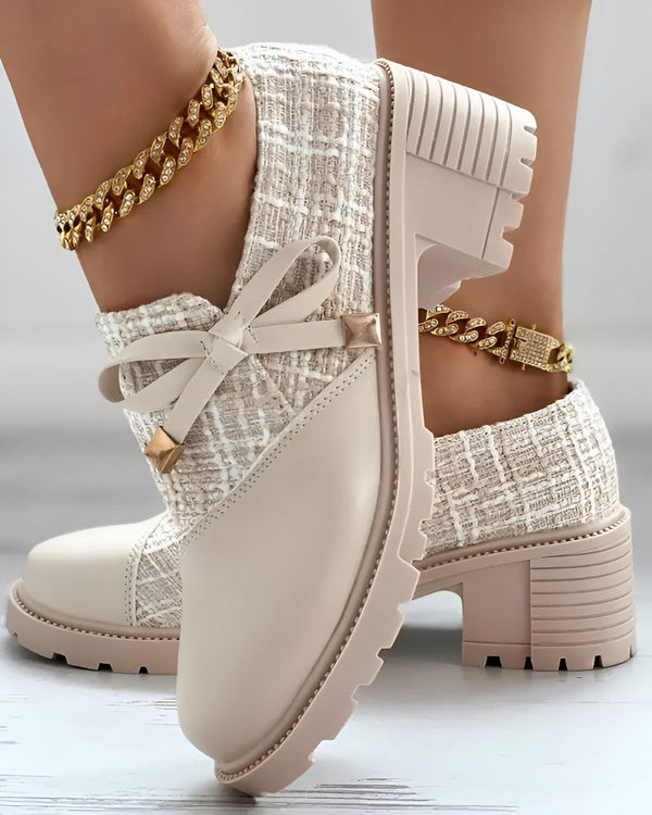 Une paire de bottines beiges à talons compensés. Les bottines sont en tweed et ont un nœud sur le devant. La personne qui les porte a une chaîne dorée à la cheville.
