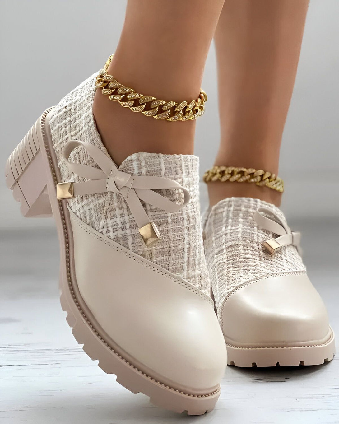 Une paire de chaussures beiges à talons compensés avec un nœud sur le devant. Les chaussures sont portées par une femme qui a une chaîne en or autour de la cheville.