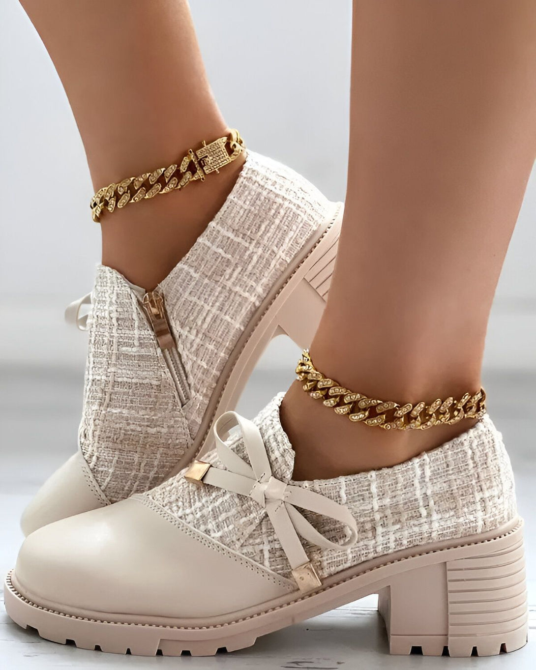 Une paire de chaussures à talons hauts de couleur beige avec un lacet et une fermeture éclair sur le côté. Les chaussures sont portées par une femme avec un jean bleu et un chemisier blanc.