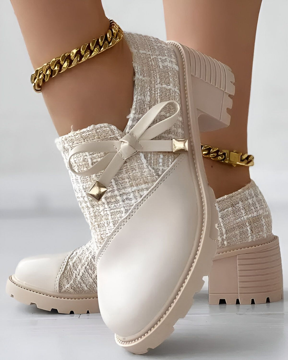 Une paire de bottes beiges à talons compensés avec un nœud sur le devant. Les bottes sont portées par une femme qui porte également une chaîne dorée autour de la cheville.