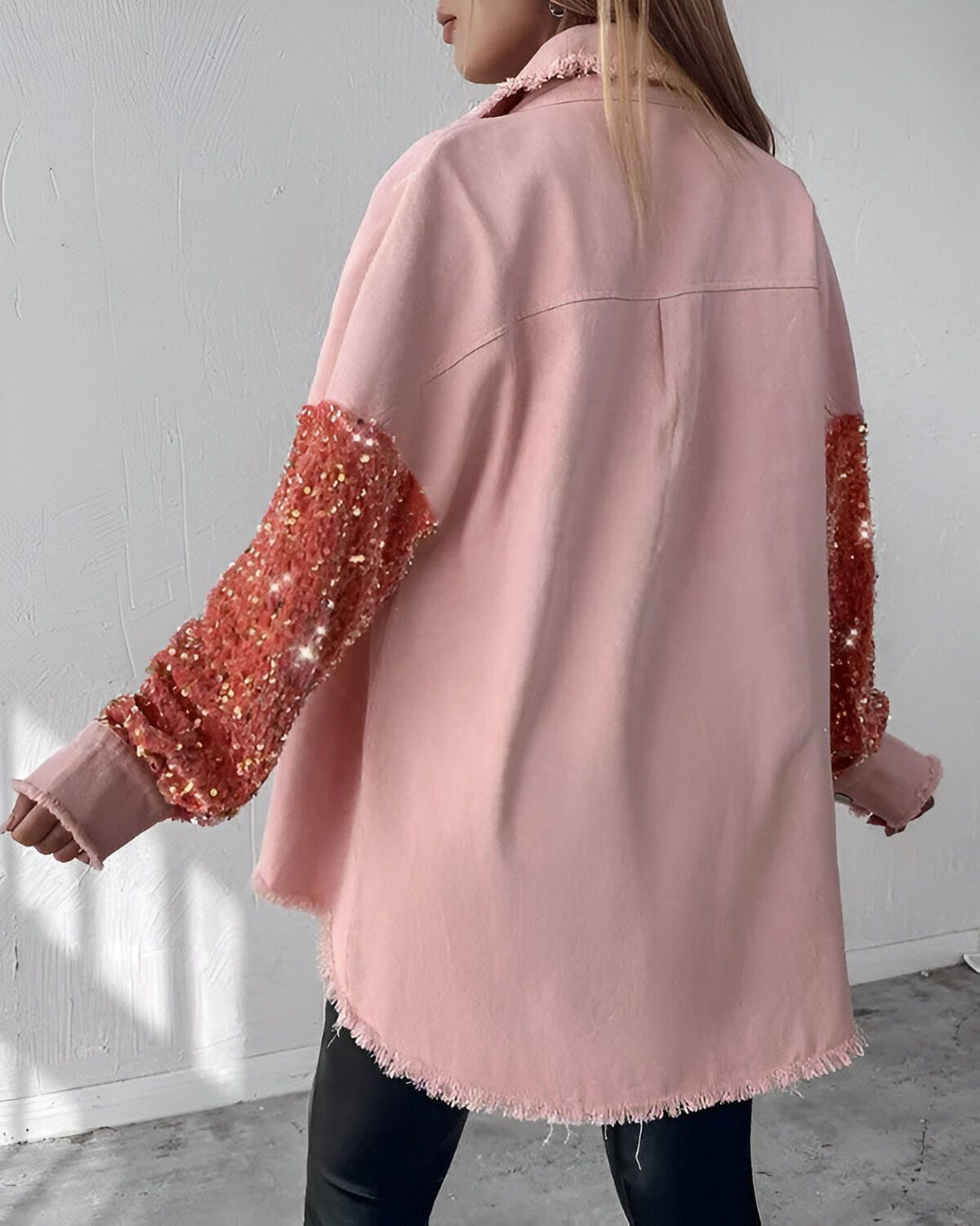 Une femme porte une chemise rose à manches longues. Les manches sont recouvertes de sequins orange. La chemise est ouverte et on peut voir un t-shirt noir en dessous. La femme est vue de dos.