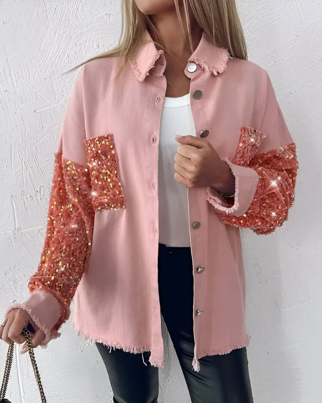 Une jeune femme porte une veste rose en jean avec des sequins oranges sur les manches. Elle est associée à un pantalon en cuir noir et un haut blanc.