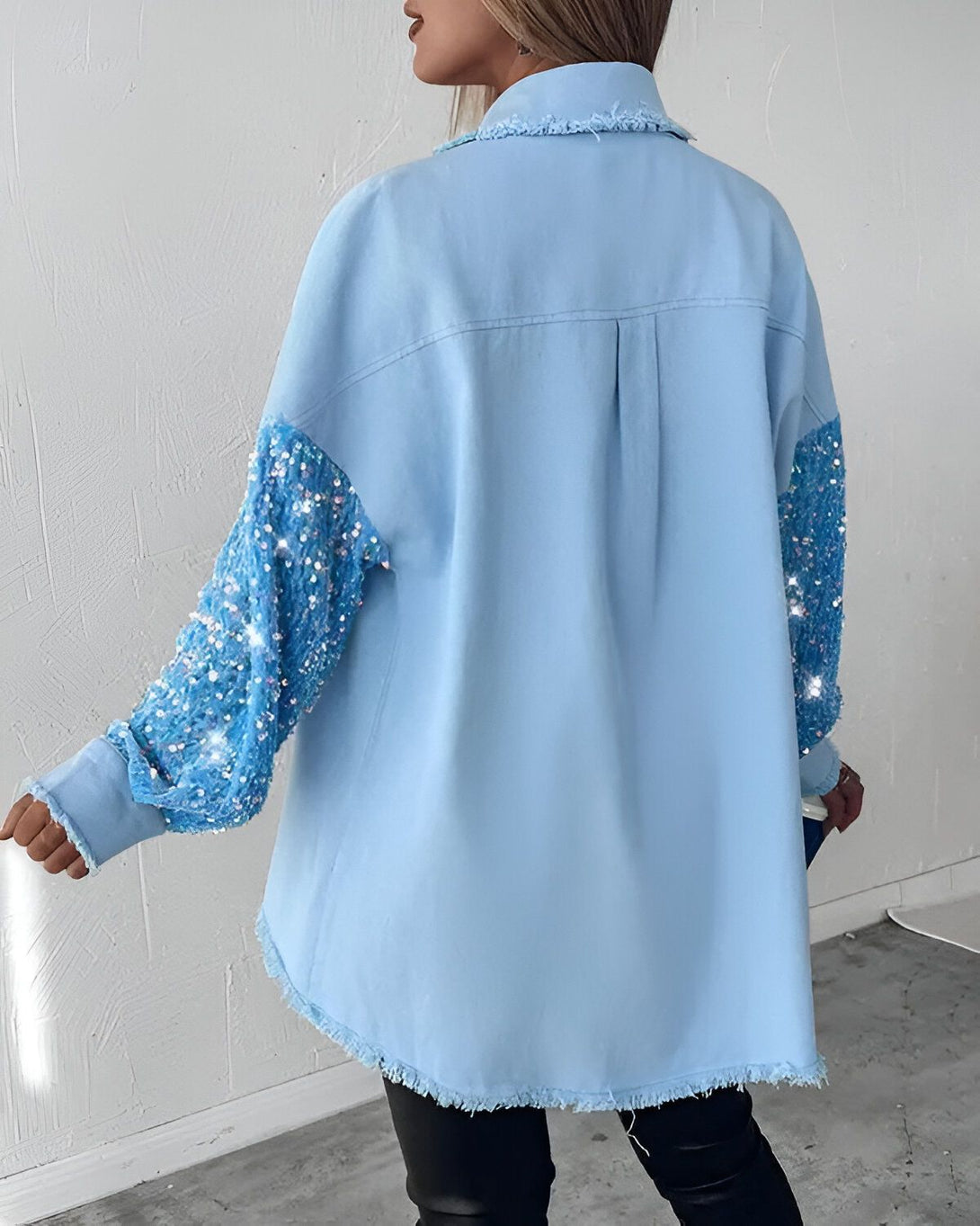Une femme porte une chemise en jean bleue avec des manches à sequins bleus. La chemise est ouverte et on peut voir un haut noir en dessous. La femme est vue de dos.
