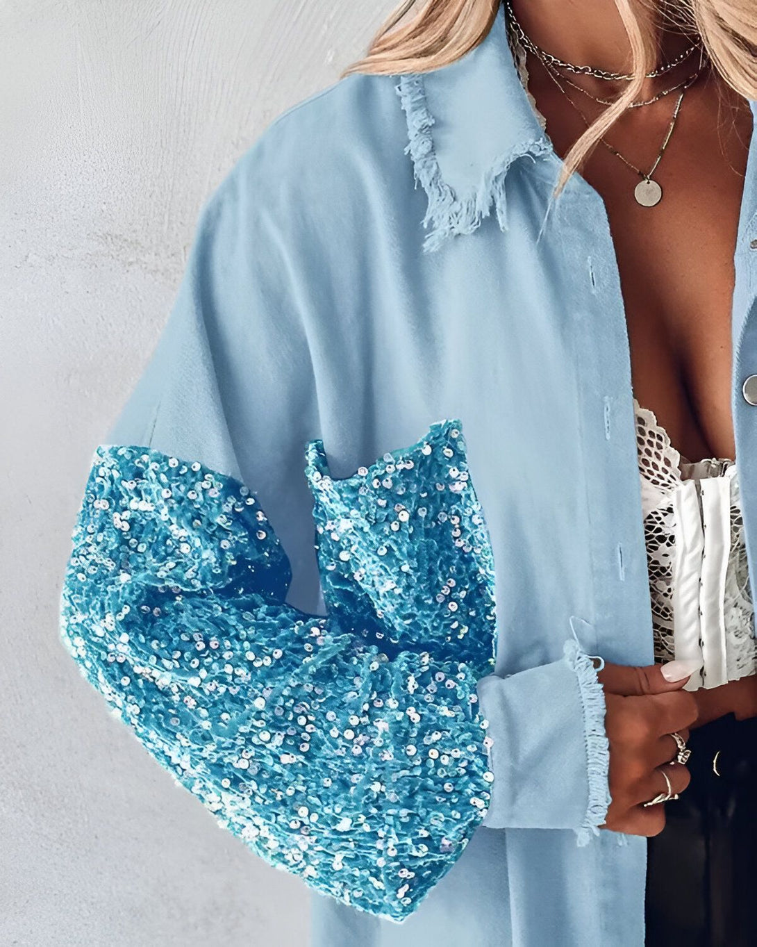 Une femme porte une chemise bleue à manches longues. La chemise est ouverte et on peut voir un soutien-gorge en dentelle blanche en dessous. La femme a les cheveux blonds et porte un collier avec un pendentif rond.