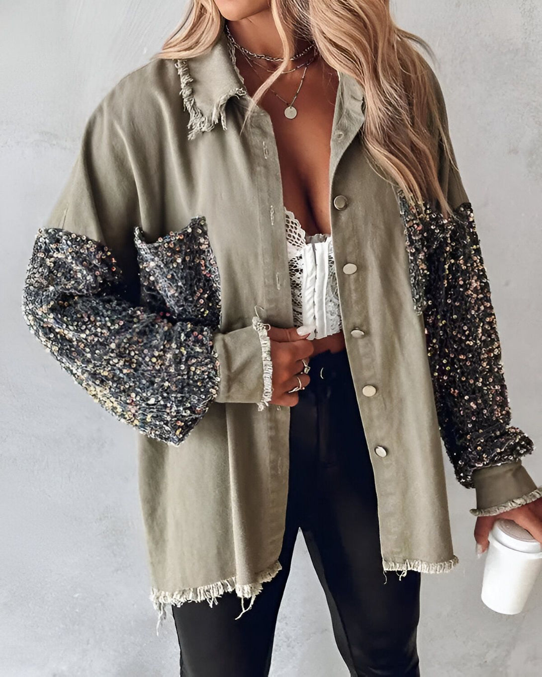 Une femme porte une veste en jean kaki avec des sequins noirs et argentés sur les manches. Elle porte également un pantalon noir et un soutien-gorge blanc en dentelle.