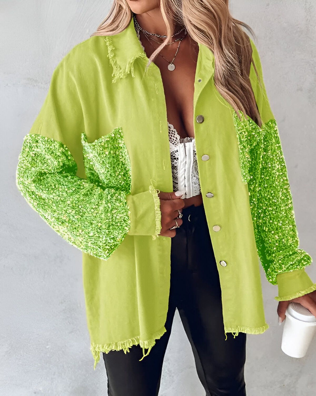 Une femme porte une veste en jean vert lime avec des sequins sur les manches. Elle est ouverte et on peut voir un haut blanc en dessous. Elle porte également un pantalon noir et des talons noirs.