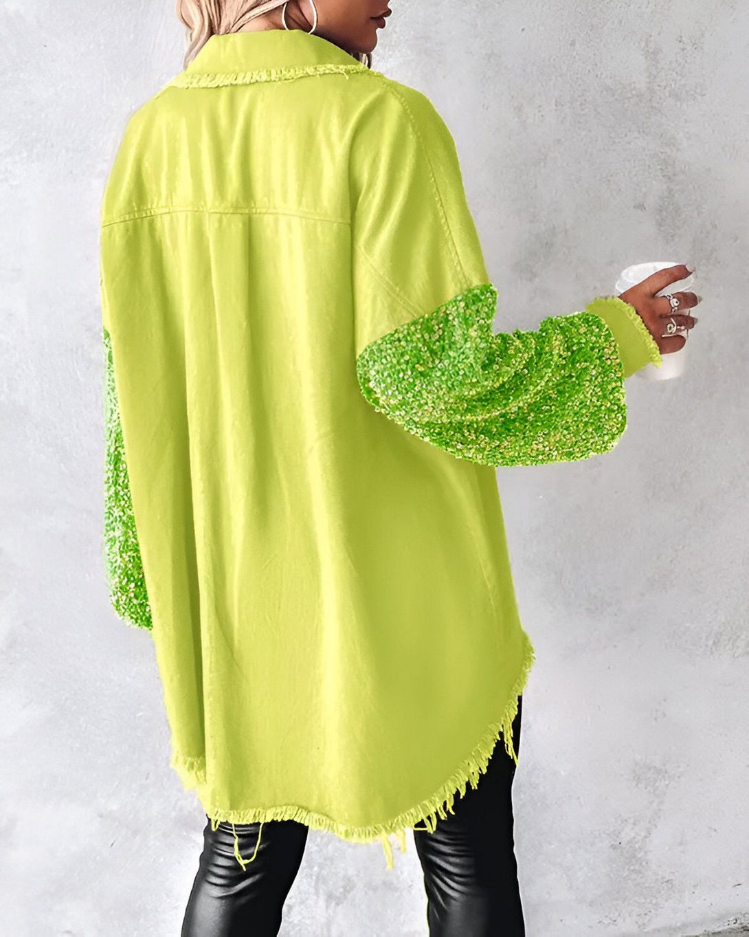Une femme porte une chemise verte en jean avec des manches à sequins verts. Elle est vue de dos et tient une tasse de café à la main.