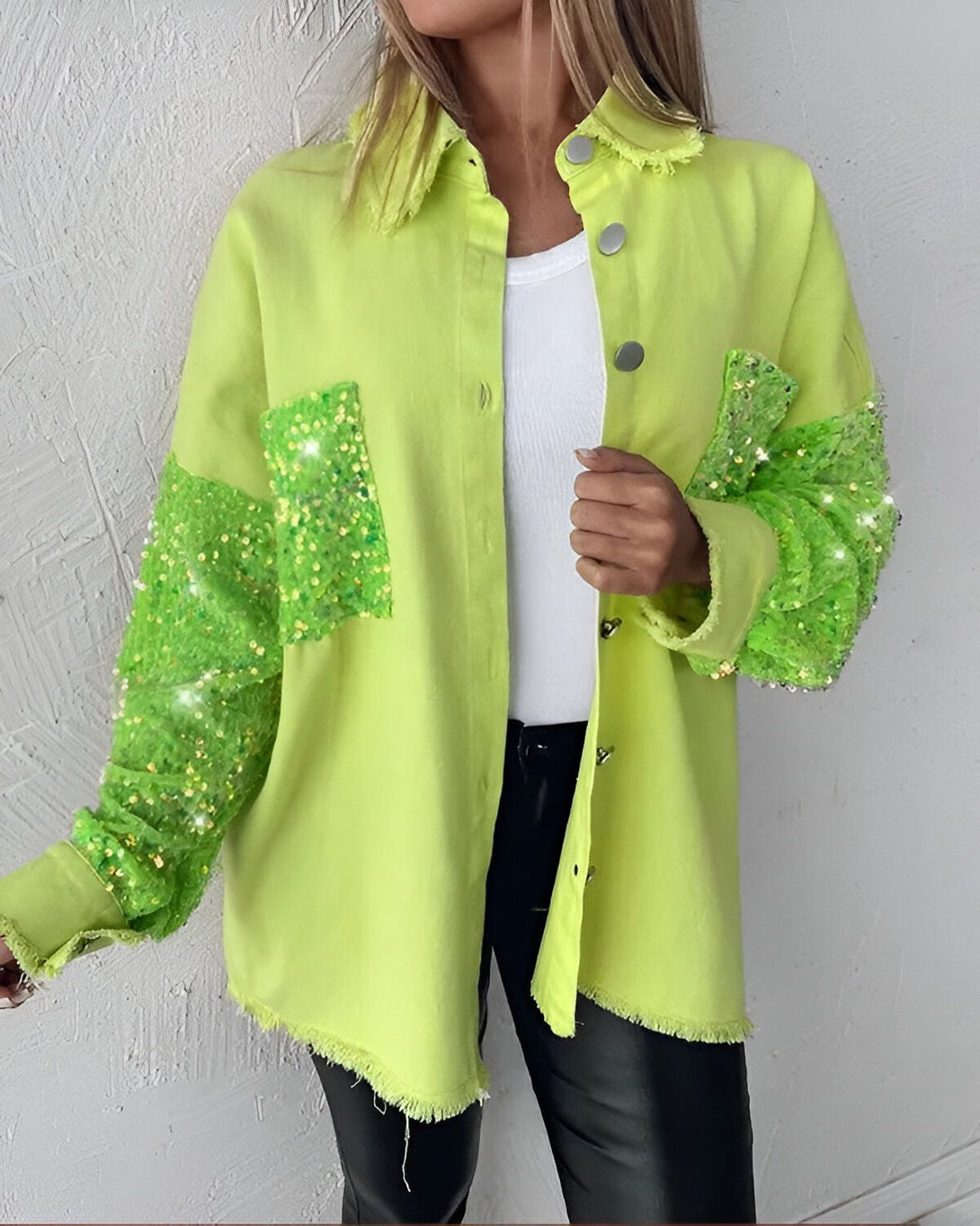 Une femme porte une veste en jean vert lime avec des paillettes sur les manches et les poches. Elle porte également un pantalon en cuir noir et un haut blanc.