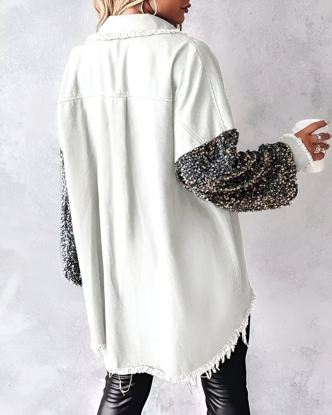 Une femme porte une chemise en jean blanche avec des manches en sequins noirs et argentés. Elle est vue de dos et tient une tasse à la main.