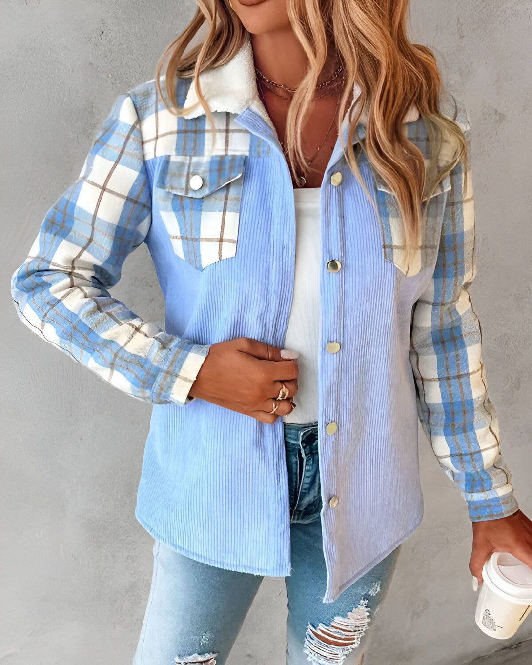 Une jeune femme porte une chemise bleue à carreaux avec un col en fourrure beige. Elle est debout et tient une tasse de café à la main.