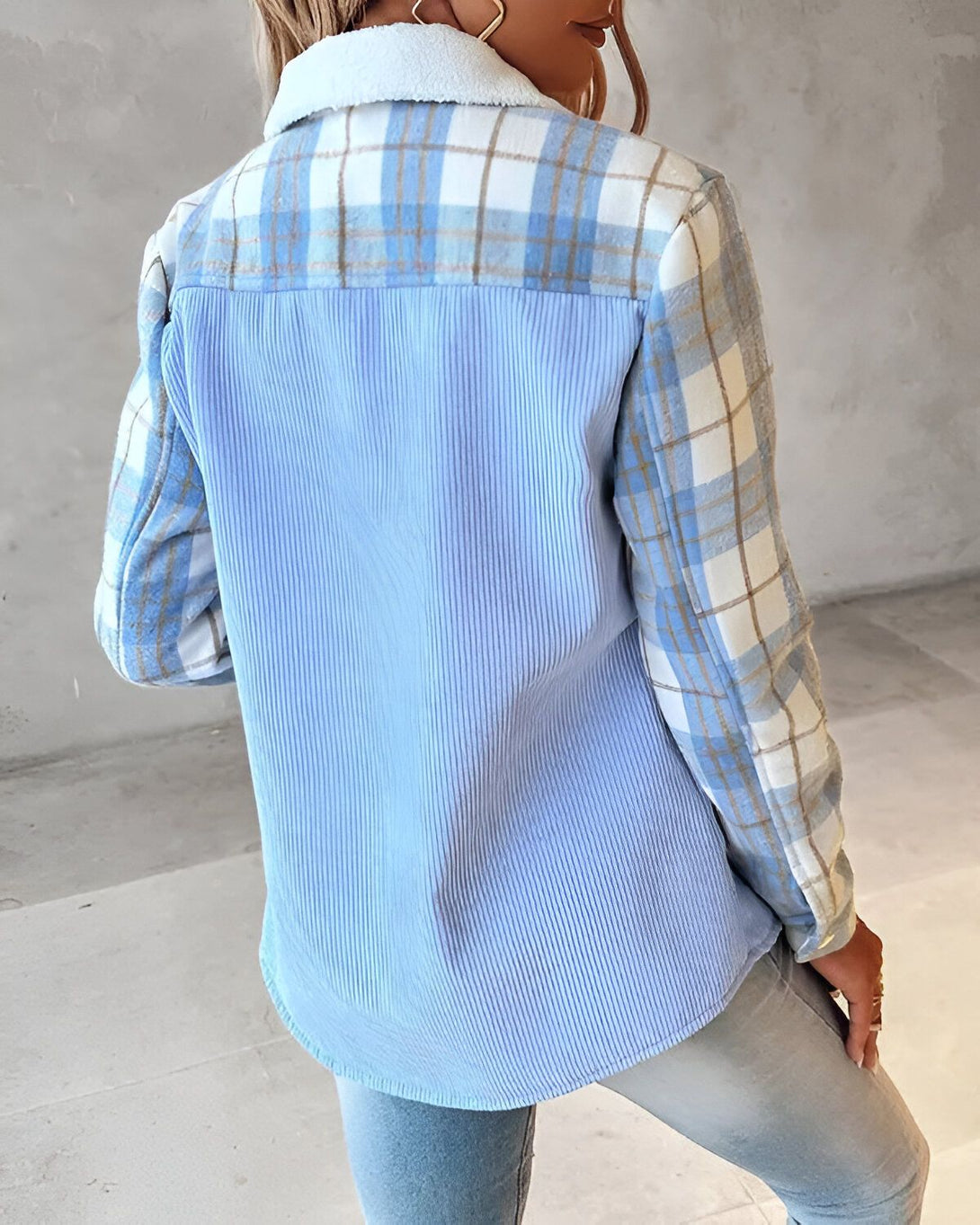 Une femme porte une chemise bleue à carreaux et côtelé. La chemise est ouverte et on peut voir un t-shirt blanc en dessous. La femme est vue de dos.