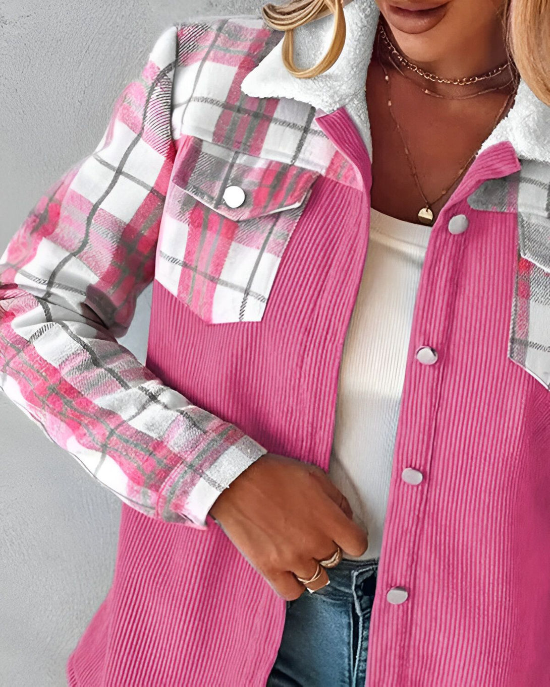 Une veste rose en velours côtelé avec des détails en tartan. La veste est ouverte, on peut voir un t-shirt blanc en dessous. Le mannequin porte également un collier et des bagues.