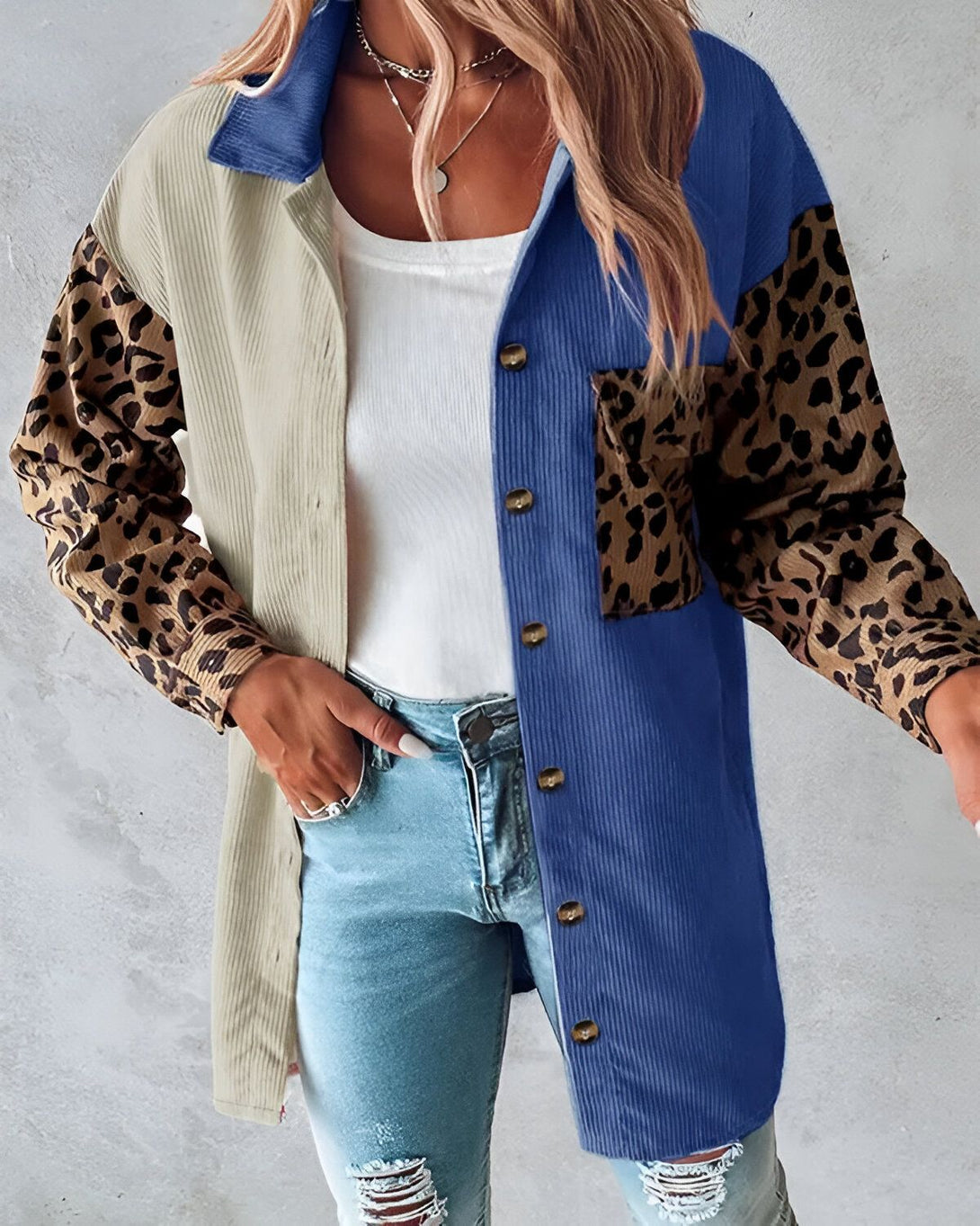 Une femme porte une chemise en velours côtelé bleu et beige avec des manches léopard. Elle est ouverte et l'on peut voir un t-shirt blanc en dessous. Elle porte également un jean bleu déchiré et des talons noirs.