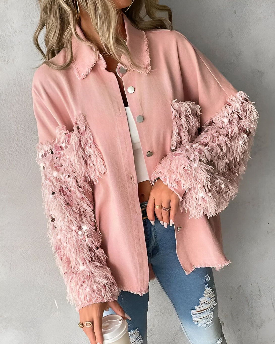 Une jeune femme porte une veste rose avec des manches en fourrure. Elle est assortie avec un jean bleu troué et un top blanc.